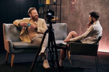 cheerful men in fashionable clothing sitting with coffee cup and discussing interview questions clipart