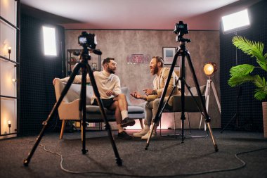 Şık stili olan neşeli, şık adamlar stüdyoda oturuyor ve röportaj sorularını tartışıyorlar.