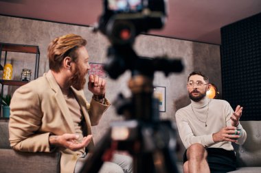 şık giyinmiş yakışıklı sakallı adamlar stüdyoda mülakat sırasında etkin bir şekilde konuşuyorlar.