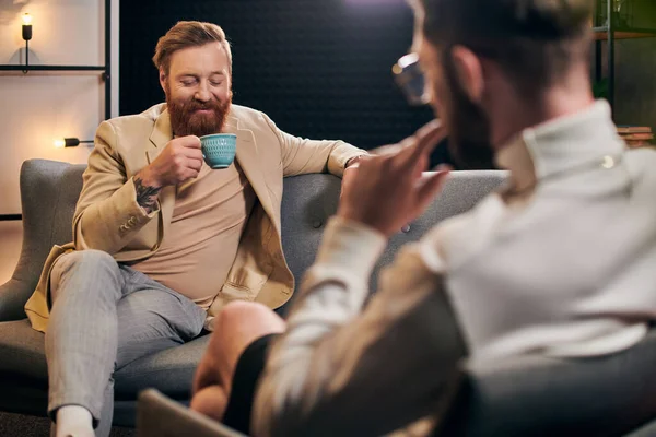 Stock image cheerful bearded man with red hair in elegant clothes sitting next to his interviewer in studio