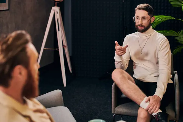 stock image attractive bearded man with glasses in elegant clothes sitting next to his interviewer in studio