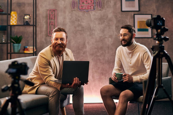 cheerful handsome men in fashionable attires with coffee and laptop smiling during interview