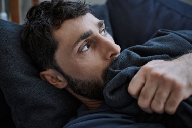 Depresyondaki sakallı adam depresyon sırasında kanepede uzanıyor, zihinsel sağlık bilincinde.
