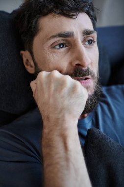 Stresli, sakallı, sıradan giyinmiş, zihinsel çöküntü sırasında elleri yüzükoyun uzanan çaresiz bir adam.