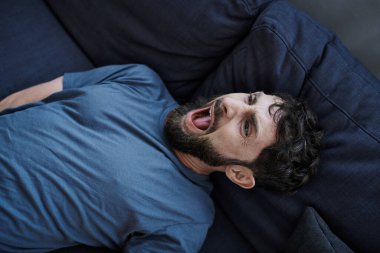 Evdeki umutsuz depresyondaki adam sinir krizi sırasında kanepede yatar ve çığlık atar. Ruh sağlığı farkındalığı.