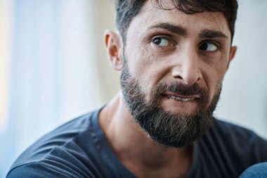 Depresyon sırasında dudaklarını ısıran sakallı hasta bir adam, zihinsel sağlık farkındalığı.