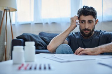 Günlük ev kıyafetleri içindeki endişeli adam kontratlara ve evraklara bakıyor ve çok endişeleniyor, akıl sağlığı için.