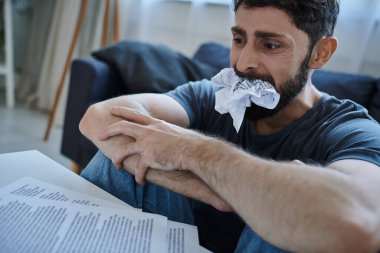 Günlük ev kıyafetleri içindeki endişeli adam kontratlara ve evraklara bakıyor ve çok endişeleniyor, akıl sağlığı için.