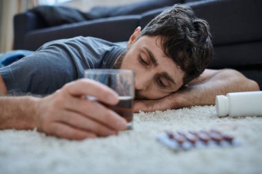 Depresyondaki adam günlük kıyafetlerini giymiş alkol içiyor ve ruhsal çöküntü sırasında haplara bakıyor.