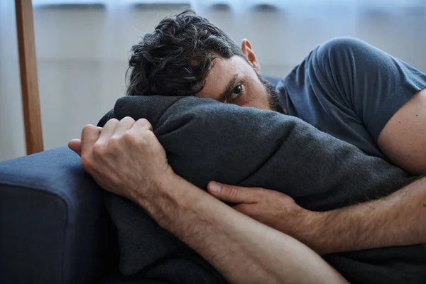 Stock image frustrated bearded man in casual home wear lying on sofa during breakdown, mental health awareness