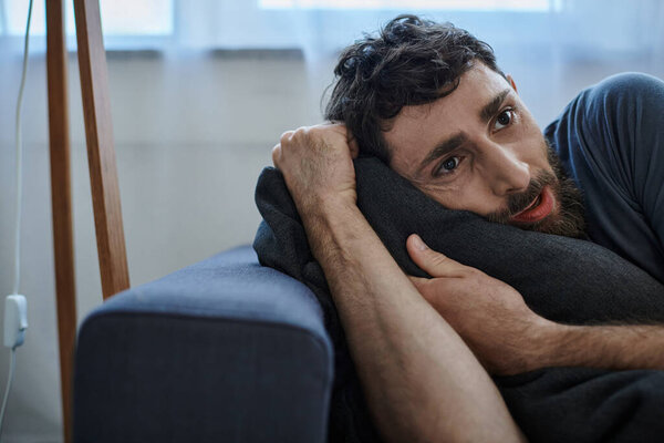 frustrated bearded man in casual home wear lying on sofa during breakdown, mental health awareness
