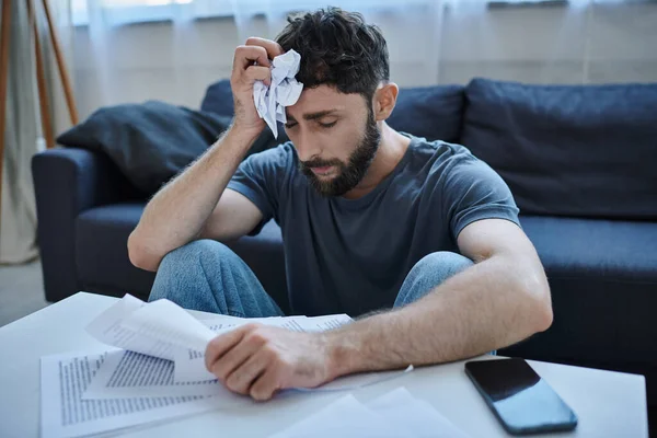 anxious man in casual homewear looking at contracts and papers and worrying a lot, mental health