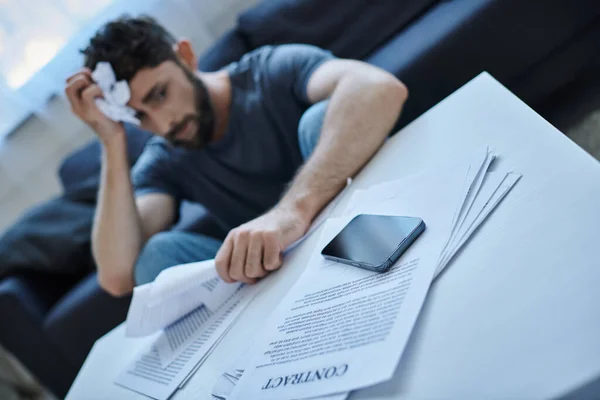 bearded suffering man in casual attire looking at contract and pills during breakdown, mental health