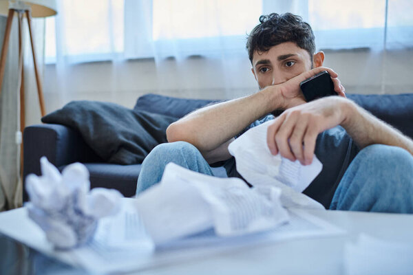 frustrated ill man in casual attire with phone and papers during breakdown, mental health awareness