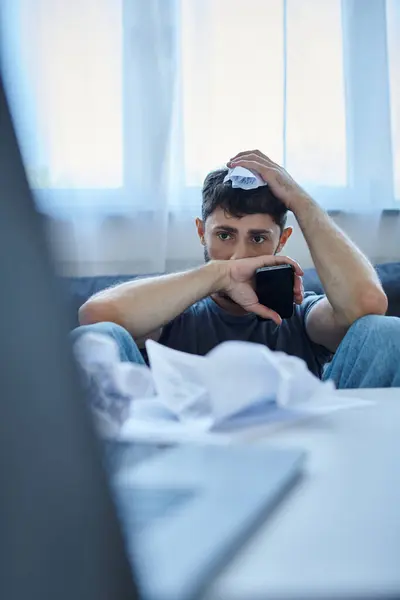 frustrated ill man in casual attire with phone and papers during breakdown, mental health awareness