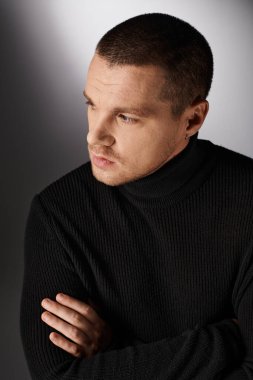 Siyah balıkçı yaka kazaklı, modaya uygun şık bir adam gri arka plana bakıyor, klasik moda.