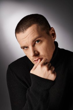 Gri arka planda kameraya bakan siyah yakalı yakışıklı bir adamın portresi.