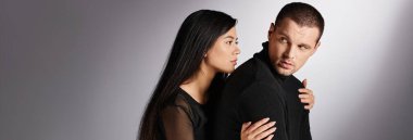 Gri arka planda kasvetli ve hayal kırıklığına uğramış adamı kucaklayan genç ve hassas Asyalı kadın, yatay afiş