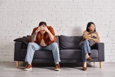 Modern oturma odasındaki koltukta oturan depresyondaki çok ırklı çift, aile boşanması kavramı.