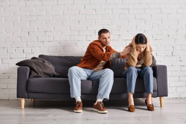 Koca sinirli Asyalı kadını sakinleştiriyor oturma odasında koltukta oturuyor, ilişki sorunları var.