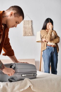 Depresyondaki Asyalı kadının yanında bavul hazırlayan genç adam yatak odasında ağlıyor, aile boşanması