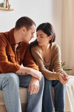 Genç ve çok ırklı bir çift yatakta oturup konuşuyor, ilişki sorunları var.