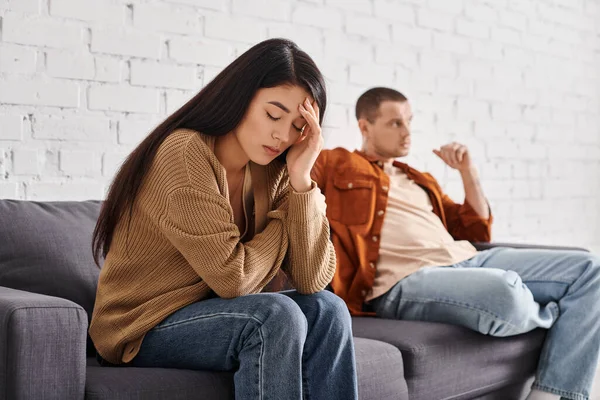 Stock image young depressed asian woman sitting with closed eyes near offended husband on couch in living room