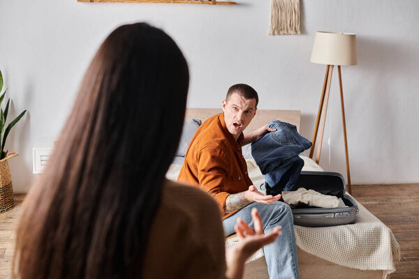 irritated man packing suitcase and quarreling with wife in bedroom at home, family divorce concept