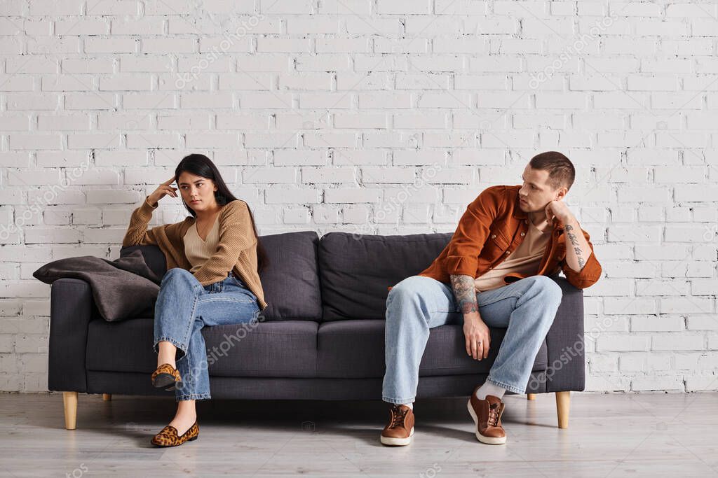 Depressed multiethnic couple sitting on couch in living room at home, family divorce concept