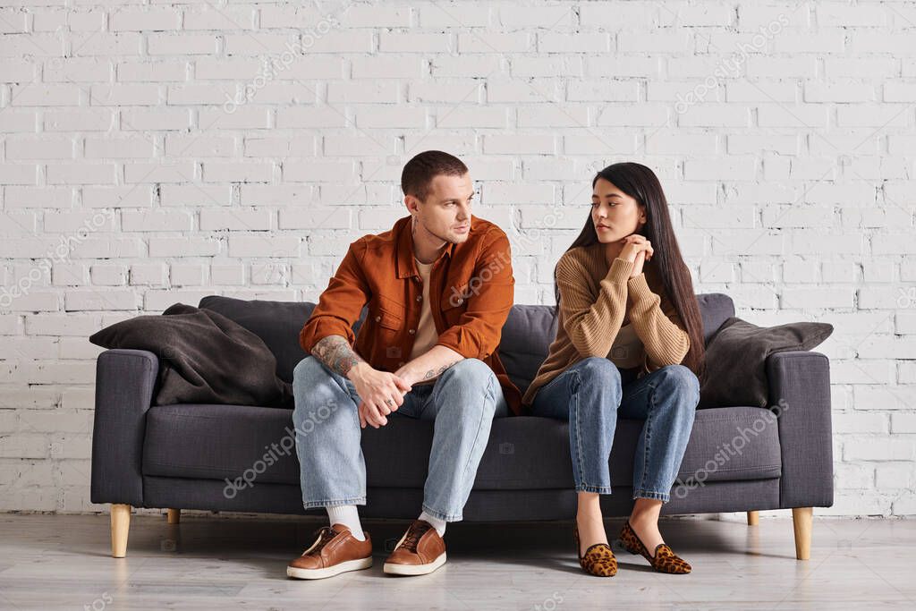 Multiethnic couple with relationship problem talking on couch in living room, divorce concept