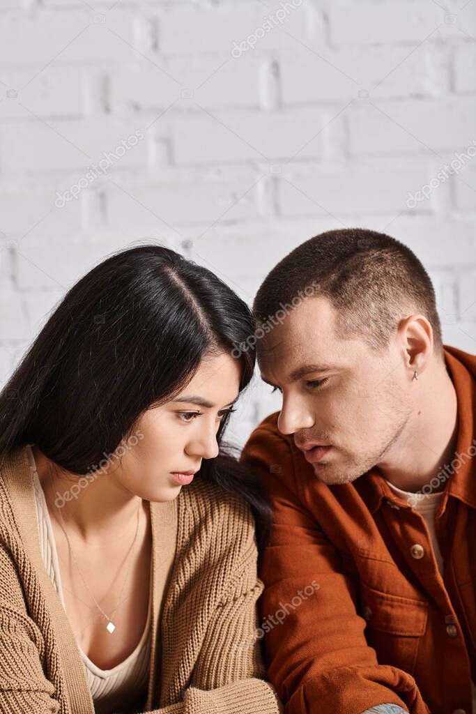 Young and depressed multiethnic couple talking in living room at home, relationship difficulties