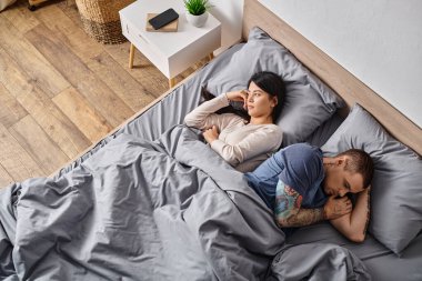 Asyalı eş ve dövmeli adamın yüksek açılı görüntüsü yatakta yatması, ilişki sorunları kavramı