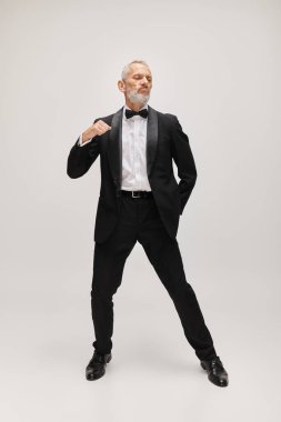 Çekici sakallı olgun adam güler yüzlü siyah smokinli papyonlu dans ederken hareket halinde poz veren