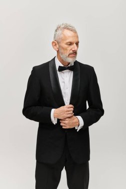 good looking bearded mature man in elegant black tuxedo with bow tie posing and looking away clipart