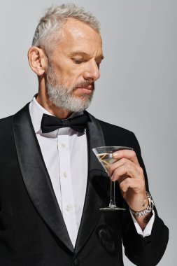 Zarif smokinli, elinde zeytinli bir bardak martini tutan çekici, sakallı olgun bir adam.