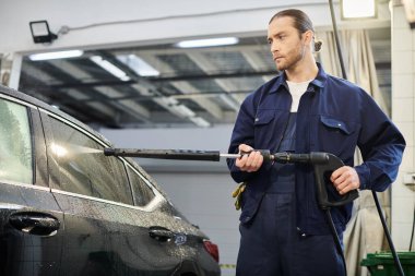 good looking dedicated serviceman in blue comfy uniform with collected hair using hose to wash car clipart