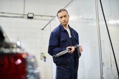 İyi görünümlü, mavi üniformalı, siyah arabayı yıkayan ve kameraya bakan çalışkan bir asker.