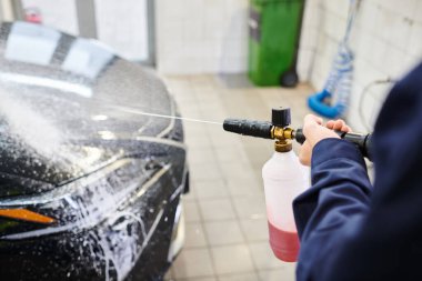 Siyah modern araba yıkamak için sabun kullanan mavi üniformalı kendini işine adamış profesyonel bir işçinin kırpılmış görüntüsü.