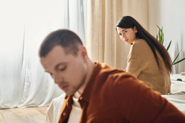 displeased frowning asian woman looking at young upset husband in bedroom at home, divorce concept
