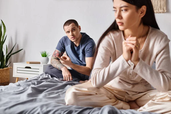 stock image young tattooed man talking to upset asian wife while sitting on bed at home, divorce concept