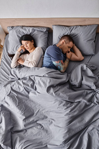 high angle view of depressed interracial couple lying down on bed at home, family divorce concept