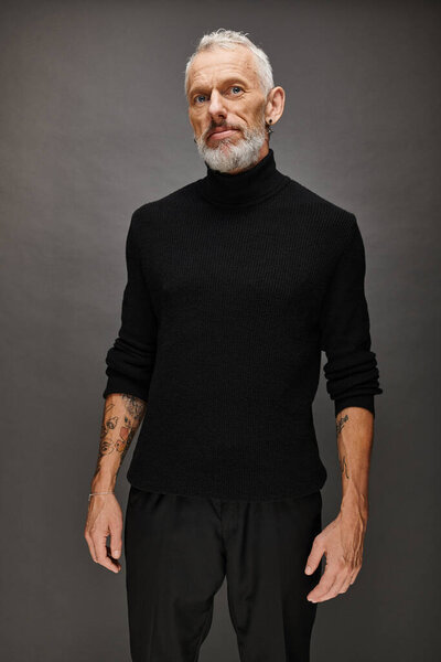 handsome fashionable mature man with beard in elegant black turtleneck posing and looking at camera