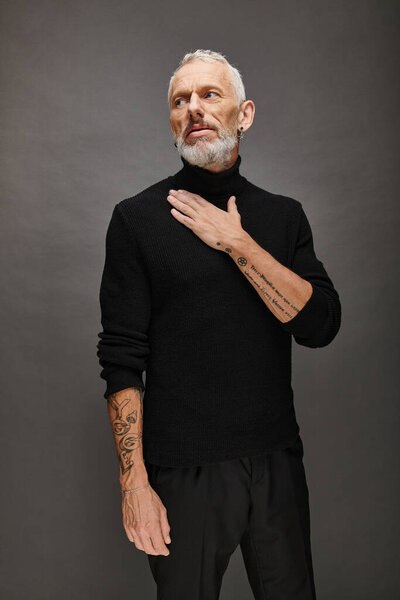 well dressed appealing mature man in voguish turtleneck posing and looking away on gray backdrop