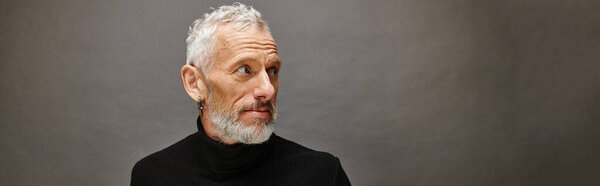 well dressed attractive mature man in voguish turtleneck looking away on gray backdrop, banner