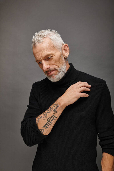 well dressed handsome mature man in chic turtleneck posing and looking away on gray backdrop