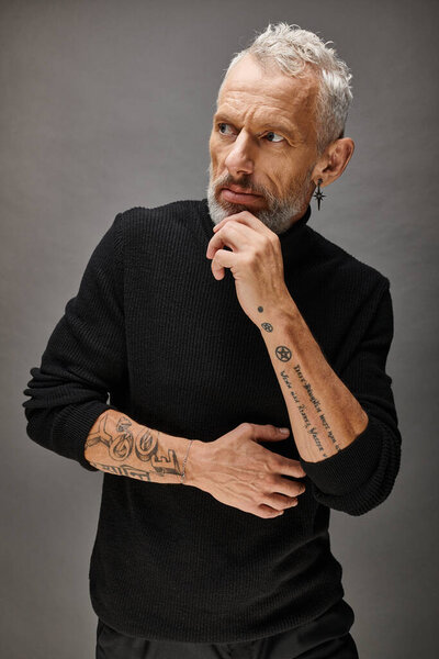 appealing well dressed mature man in trendy turtleneck posing and looking away on gray backdrop