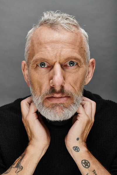 portrait of attractive bearded mature male model in fashionable black turtleneck looking at camera