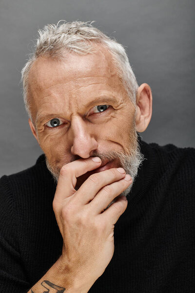 portrait of handsome bearded mature male model in fashionable black turtleneck looking at camera