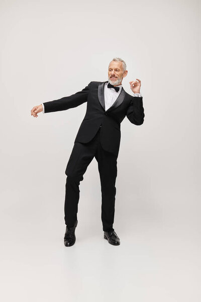 attractive happy mature man with gray beard and bow tie in elegant tuxedo dancing actively