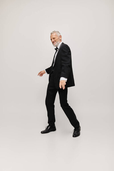 appealing joyous mature man with elegant dapper style with beard dancing happily on gray backdrop